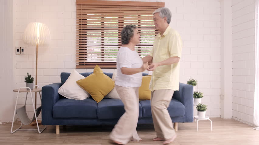 Asian elderly couple dancing together while listen to music in living room at home, sweet couple enjoy love moment while having fun when relaxed at home. Lifestyle senior family relax at home concept. Royalty-Free Stock Footage #1023392785