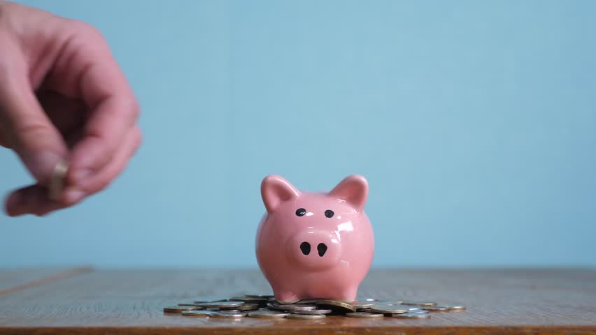 Piggy bank saving business standing on a pile of coins concept. A hand is putting a coin in piggy bank. saving money is an investment for the future. Banking investment  business  | Shutterstock HD Video #1023393757