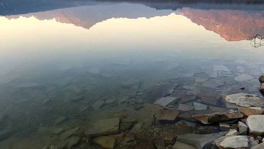 Slow motion of stone falling on the surface of a lake where the mountains are reflected