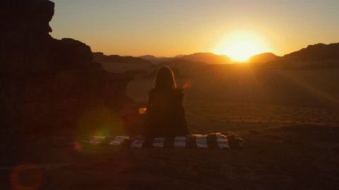 Amazing Sunset on Desert Wadi Rum, Girl is sitting on carpet and she is resting. Landscape of Red Desert Wadi Rum in Jordan. 