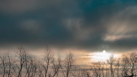 Gloomy and dramatic sky over the treetops. The disk of the rising sun through the thick and dark clouds. Time lapse video