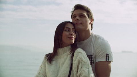 Loving Italian boyfriend holds his girlfriend as they look up from a pier to the buildings and coast of the Amalfi Coast, with bright sunny light. Medium to wide shot on 8k helium RED camera