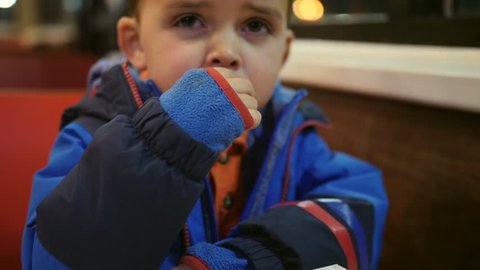 A toddler boy eats fast food french fries in a restaurant