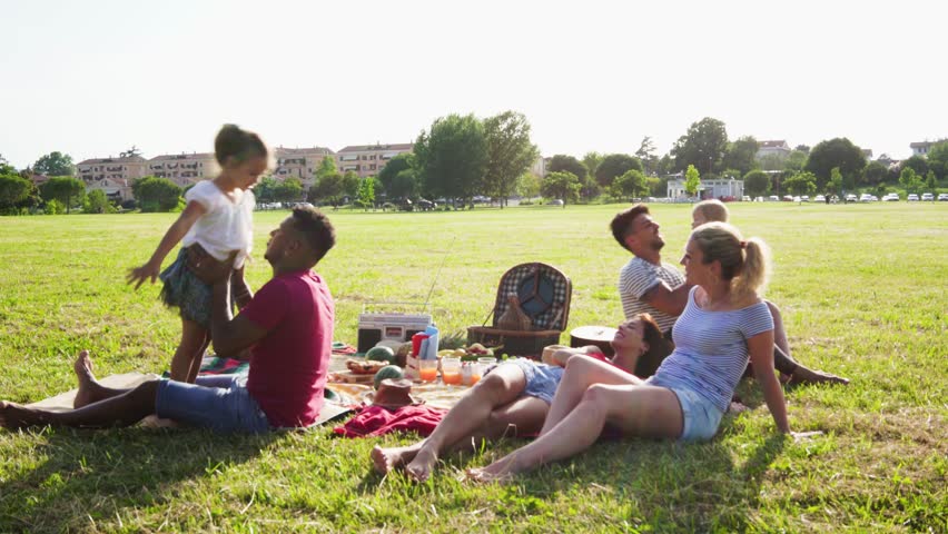 Happy families doing pic-nic in pubblic park outdoor - Young parents having fun with children in summer laughing together outside - Positive mood, parenthood, childhood and food concept Royalty-Free Stock Footage #1023404293