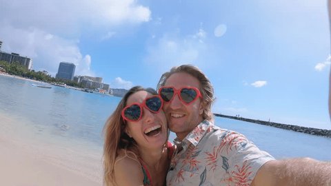 Selfie of couple with heart shaped sunglasses on beach in Hawaii. Young lovers taking a selfie on Waikiki Beach in Honolulu. Hawaii USA. Girl kisses man on cheek