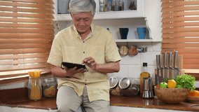 Portrait asian senior man using tablet searching online shopping. Sharing social media communication in kitchen at home.