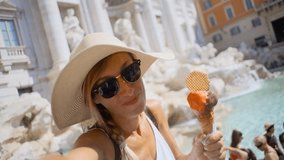 Girl with Italian gelato Ice cream taking selfie at Trevi fountain in Rome Italy; Caucasian female enjoying Summer vacations in European capital city  