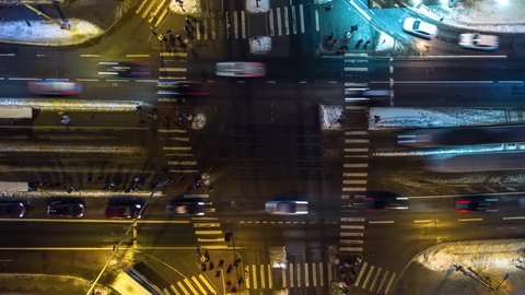 Busy intersection night aerial timelapse with pedestrians, cars, trams and buses. Aerial top-down view of an intersection with heavy rush hour city traffic