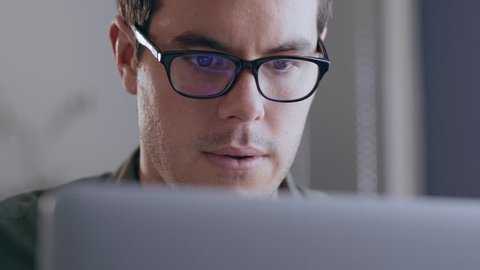 Close up of a young, caucasian businessman working on his laptop in a modern office