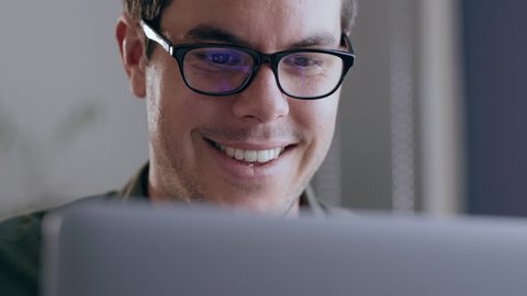 Close up of a young, caucasian businessman happily working on his laptop in a modern office