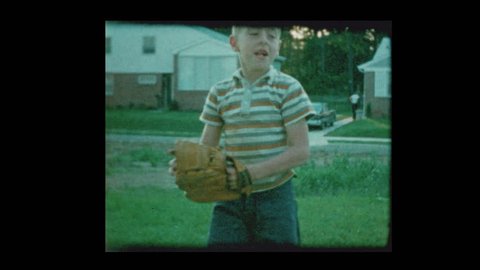 1960 Young blond boy playing catch with baseball in suburban backyard