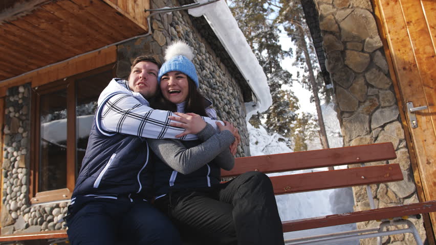 Happy loving couple sitting on a bench near the winter Chalet in the mountains.