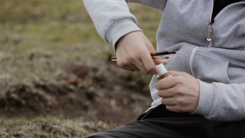Hands of an Anonymous School Boy holding Paint Brushes and Opening Paint Jar Outdoors. Close Up.  