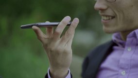 Cropped shot of young man talking on smartphone. Male hand holding smartphone on blurred natural background. Communication and technology concept