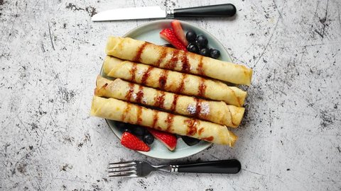 Plate of delicious crepes roll with fresh fruits and chocolate placed on rusty table. Top view, flat lay.