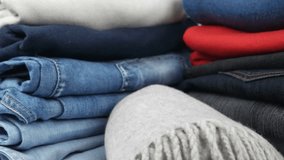 Stacks of blue and dark jeans, multi-colored sweaters and warm gray scarf, background