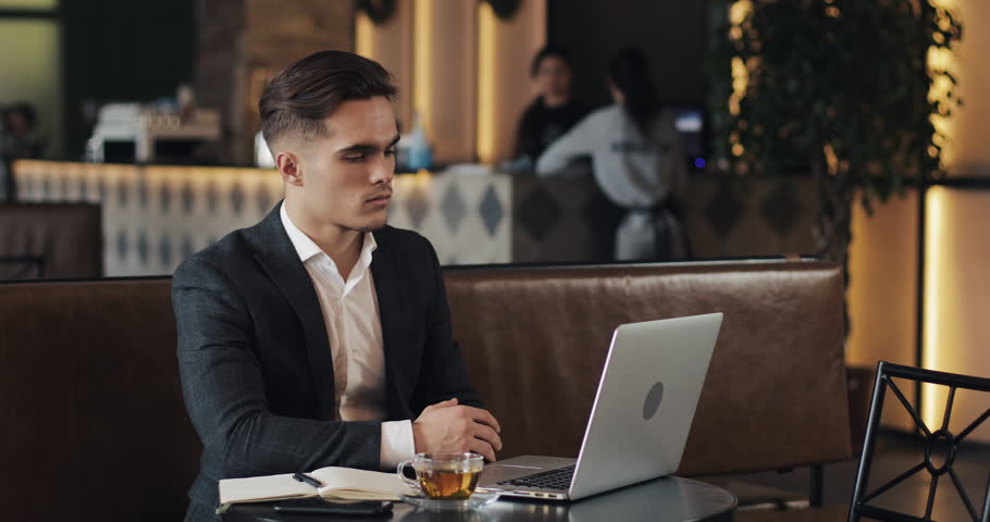 Portrait of young successful businessman sitting in cafe with laptop and looking into the camera | Shutterstock HD Video #1023459739