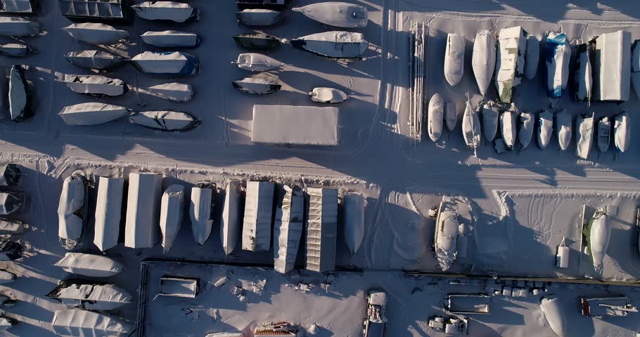 Flying with a drone straight above boats that are on land for winter storage on snowy winter day, Espoo Finland