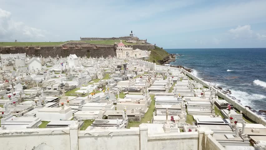 AERIAL: Flying over the grave stones on Santa Maria cemetery in San Juan, with the Felipe castle in the background and waves clashing from the sea.