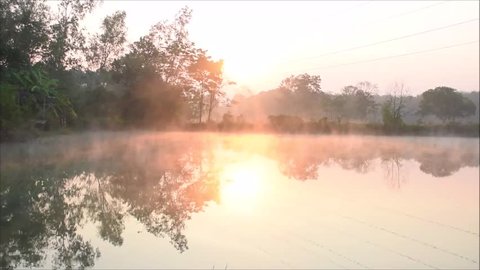 The fog evaporates above the water surface in the morning in winter, Peaceful sunrise besides the pond in the morning in Thailand, Quiet morning with golden light from sunrise, Landscape nature view
