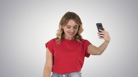 Cheerful female blogger recording video to front camera of modern telephone while walking on gradient background.