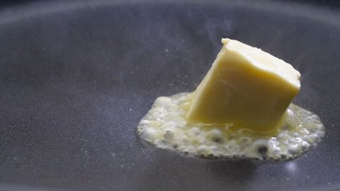Butter melting sizzling in frying pan on stove. Close up.
