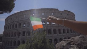 Pov personal perspective of human hand holding Italian flag stretching towards the Coliseum in Rome, Italy 