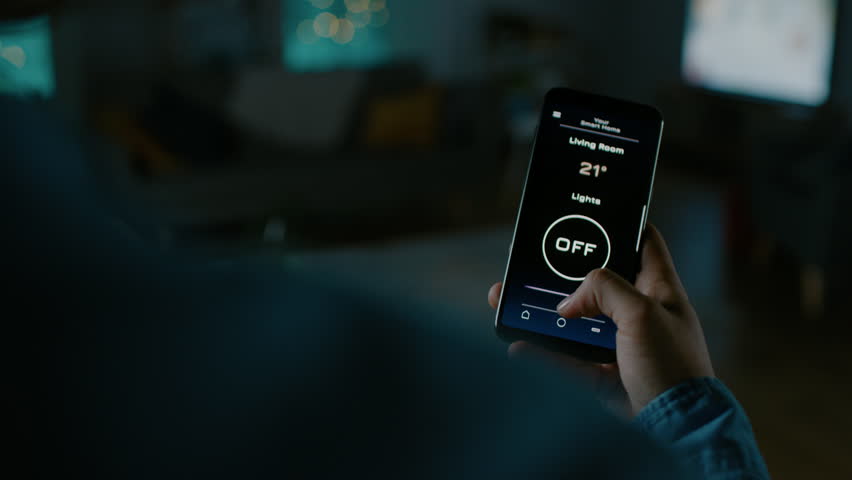 Close Up Shot of a Smartphone with Active Smart Home Application. Person is Tapping the Screen and Light is Being Turned On in the Room. It's Cozy Evening in the Apartment. Royalty-Free Stock Footage #1023495709