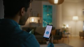 Young Handsome Man Gives a Voice Command to a Smart Home Application on His Smartphone and Lights in the Room are Being Turned On. It's a Cozy Evening. - Powered by Shutterstock - Get 15% off with code: PIKWIZARD15