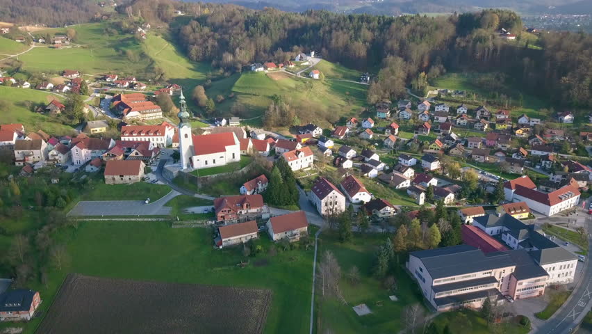 Aerial: Flying over catholic church with big parking place beside. Filming small village on beautiful spring sunny day.