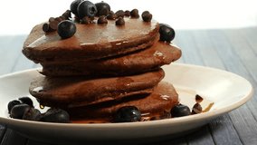 pouring maple syrup on cacao pancakes pile, blue background, close up