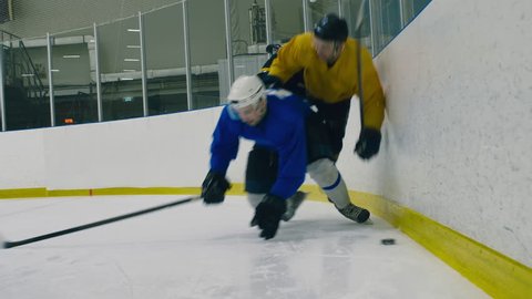 Track out shot of professional hockey player bumping into his opponent and pressing him to arena's barrier to take puck away