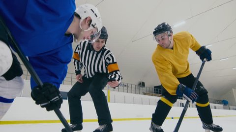 Down shot of referee throwing puck to face-off, after which ice hockey players starting to play and skating away from camera