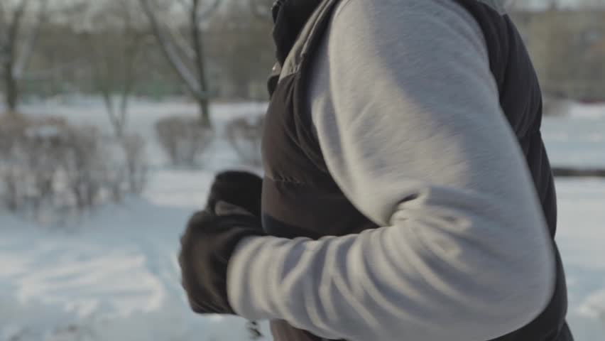 A man runs in the winter, side view, a large shot of hands, in the background are trees