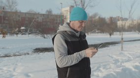 A man looks into the smartphone in the winter on the street, the camera moves in a semicircle