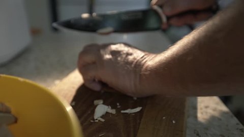 old man's hand close-up shreds mushrooms on a wooden board with a large black kitchen knife