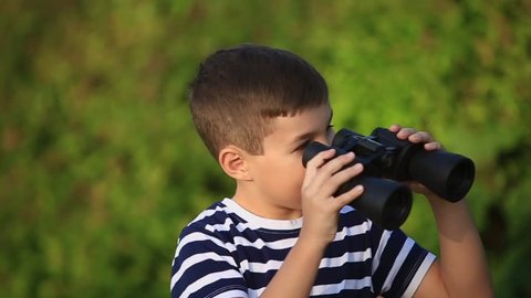 Little boy walking in the park and looking through binoculars