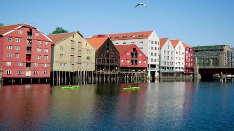 Trondheim, Norway-July 27, 2018: Beautiful bright and colorful houses on wooden stilts are built in a row in the water of the bay on a sunny summer day. People swim in kayaks