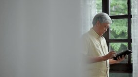 Portrait asian senior man using tablet searching online shopping. Sharing social media communication beside window at home.