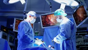 European male Caucasian surgical team in scrubs training performing Laparoscopy surgery on the patient in operating theatre using video camera technology 