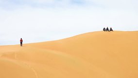 woman making photo of friends sitting on sandy dune hill