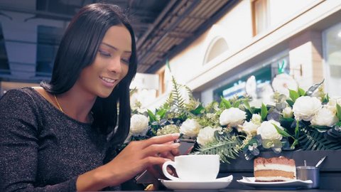 Young attractive Asian girl, ladyboy is smiling and using her smartphone while sitting at a table in a coffee shop