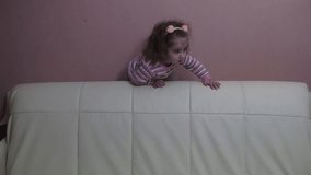 Little girl with curly hair frolics on the couch. Video full hd.