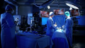 Laparoscopy surgical operation transmitted on hospital monitors being performed by Multi ethnic female training as surgeon wearing surgical gloves and scrubs RED DRAGON