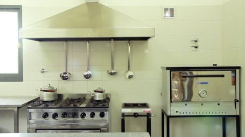 Empty School Kitchen Interior with Range Hood and Kitchen Utensils hanging on a Wall.