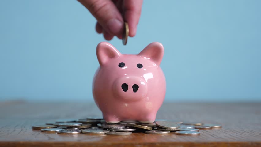 Piggy bank business standing on a pile of coins concept. A hand is putting coin in a piggy bank on a yellow background. saving money is an investment for the future. Banking investment and lifestyle | Shutterstock HD Video #1023549208