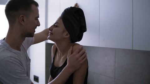Young romantic couple on the kitchen. Sexy young woman is sitting on the counttable in domestic clothes and bath towel on head and hugging her handsome man. Spending time together, hugging. Passionate
