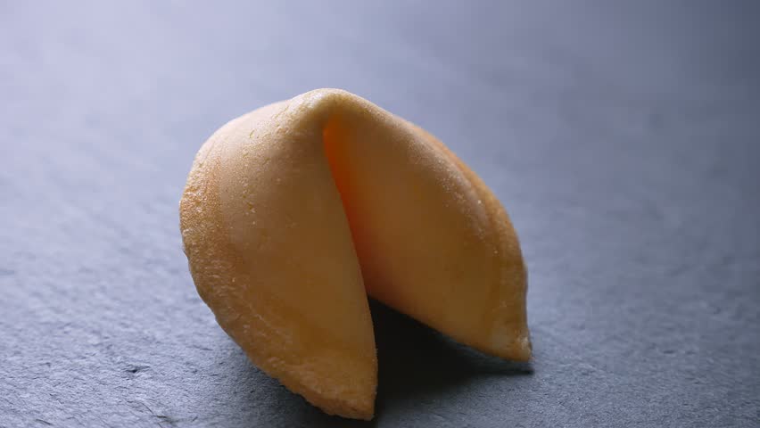 Close-up circling around shot of fortune cookie spinning slowly on gray table background.