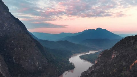 Aerial: flying over Nam Ou River Nong Khiaw Muang Ngoi Laos, sunset dramatic sky, scenic mountain landscape, famous travel destination in South East Asia. Flat d-cinelike color profile.