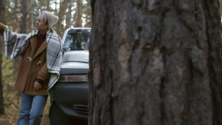 Zoom in shot of young Caucasian woman in beanie posing for smartphone camera while taking selfie in forest